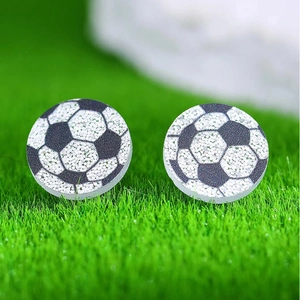 Détail de boucles d'oreilles ballon de foot avec paillettes sur fond d'herbe artificielle