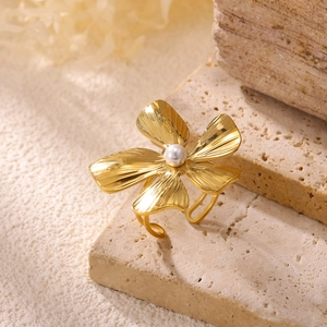 Macro shot of gold floral ring with centered pearl on a textured stone base
