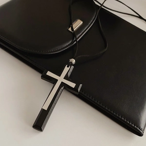 Macro detail of a double layer wood and metal cross pendant on black leather cord
