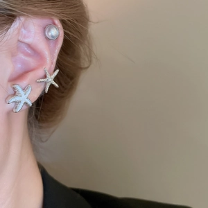 Macro view of starfish studs and pearl earrings set on ear with fine metal textures