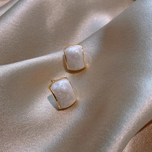 Detailed close-up of square pearl earrings on silk fabric with gold metal plating