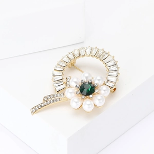 Elegant gold flower brooch with green gemstone, pearls, and crystals on a white pedestal