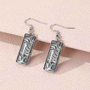 Macro shot of rectangular silver earrings featuring black and white marble fluid art design
