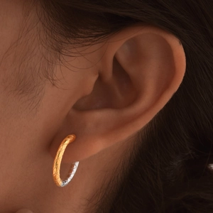 Close-up of gold and silver plated hoop earrings with engraved diamond pattern on model