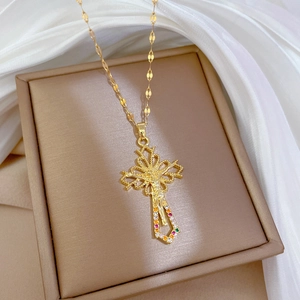 Detailed view of a gold cross necklace featuring colorful gemstones on a beige jewelry box