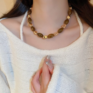 Detail of a brown resin oval pendant and gold beads necklace on a white sweater background