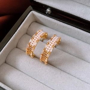 Detail of 18K gold C-shape earrings with pearls and crystals on gray velvet box