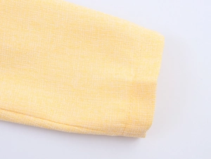 Dettaglio ravvicinato della trama in tweed giallo e del polsino di una giacca corta chic