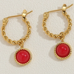 Detail of gold twisted hoop earrings with round red gemstone pendants on white surface