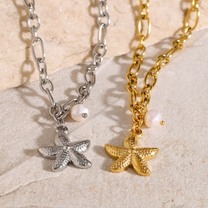 Close-up of 18k gold and silver starfish pendants with white pearls on a textured stone base