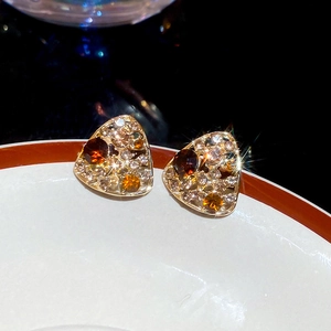 Macro shot of gold triangle stud earrings with amber and white crystals on white ceramic