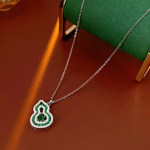 Close-up of emerald and white zircon gourd pendant on silver chain over green stand