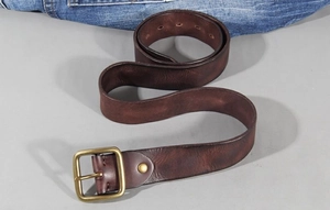 Close-up of vintage brass buckle on premium dark brown leather belt with denim jeans