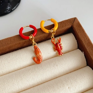 Close-up of golden stainless steel hoop earrings with red enamel lobster charms on velvet
