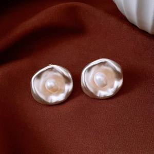Primer plano de pendientes retro dorados de forma irregular con elegante perla central.