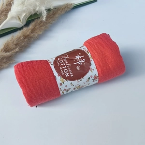 Detail of a rolled pleated orange-red cotton scarf with floral branded paper packaging