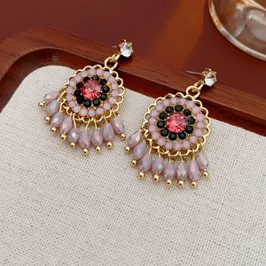 Macro detail of gold-tone floral earrings with pink crystal and purple bead tassels