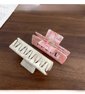 Detail view of large acetate hair claws in marble white and floral pink on wood