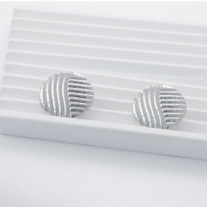 Macro shot of silver circular earrings with hammered and striped texture on ceramic tray