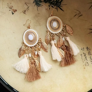 Detail of bohemian gold earrings with leaf charms and soft cotton tassels on a decorative tray