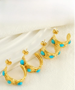 Détail de boucles d'oreilles C dorées vintage avec turquoise et textures radiales