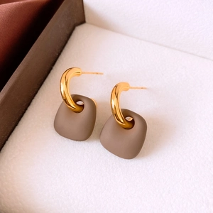 Detail of gold geometric hoop earrings with matte brown trapezoid charms in a jewelry box