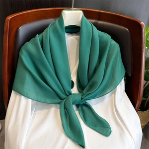 Detail of a lightweight green cotton linen scarf knotted over a white shirt on a chair
