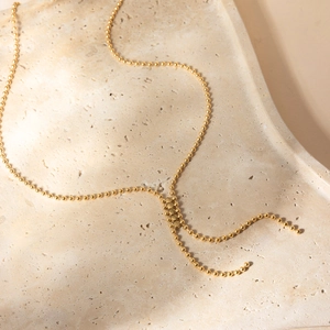 Détail d'un collier en Y à billes dorées posé sur un plateau en pierre texturée