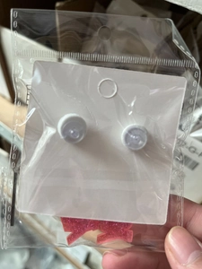 Detailed view of pink glitter bow earrings and white studs in protective packaging