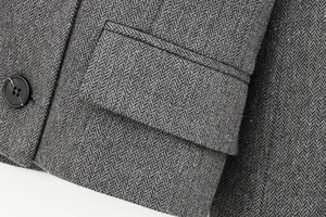 Detailed macro view of grey herringbone fabric blazer featuring pocket and dark button