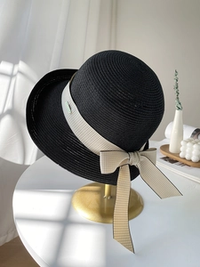 Détail d'un chapeau de paille noir avec ruban à carreaux beige et petit logo métallique
