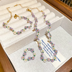 Handmade seed bead jewelry set with purple floral patterns on wooden display