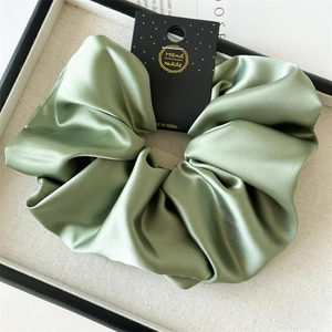 Close-up of sage green satin scrunchie with smooth silk texture and handmade card