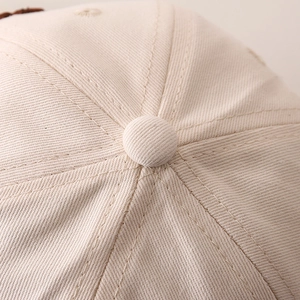 Dettaglio delle cuciture in cotone e del bottone superiore del cappellino beige da bambino