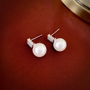 Macro shot of elegant round pearl earrings with cubic zirconia inlay on red silk