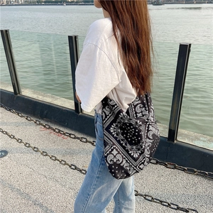 Outdoor shot of a black paisley canvas tote bag carried by a model near a riverbank