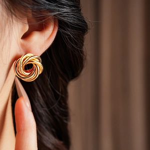 Close-up of model wearing gold geometric knot earrings with intertwined metal design