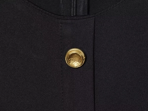 Détail d'un bouton en métal doré texturé sur le tissu d'une robe midi noire