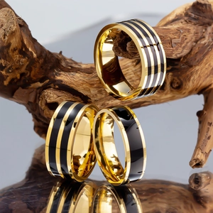 Modern gold-plated stainless steel rings with black enamel stripes displayed on a wooden stand
