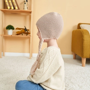 Detail of light beige knitted baby hat with long braids and soft warm ear flaps