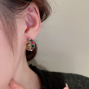 Macro shot of chunky gold C-shaped hoop earrings with colorful pavé rhinestones