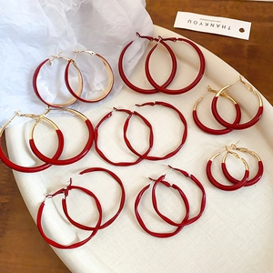 Detail view of various sizes of red hoop earrings with gold finish and smooth lacquer texture