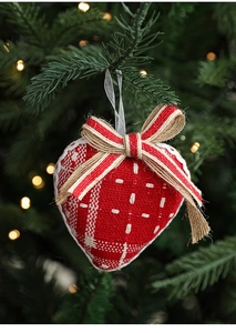 Detail of a red burlap heart ornament with a rustic bow hanging on a lit Christmas tree