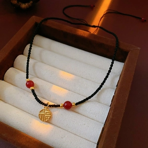 Detail of hand-woven black cord necklace with Fu character pendant and red agate beads