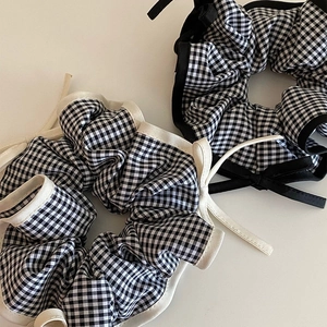 Close-up of two gingham pattern scrunchies with black and white fabric and delicate trim