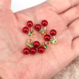 Detailed view of cherry-shaped enamel charms with gold rings for DIY jewelry making