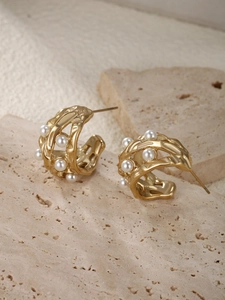 Detailed view of C-shaped gold molten lava earrings with white pearls on a stone surface