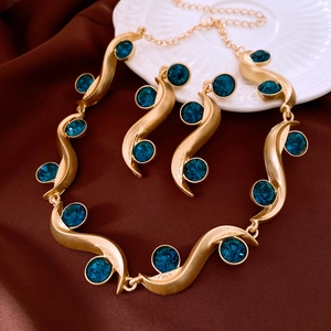 Detailed shot of gold necklace and earrings set with blue crystals on brown silk