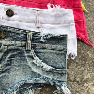 Dettaglio di pantaloncini di jeans a vita bassa con orlo sfrangiato e bottoni metallici