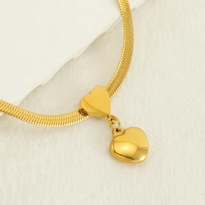 Collier à chevrons doré en acier inoxydable avec pendentif cœur sur fond texturé